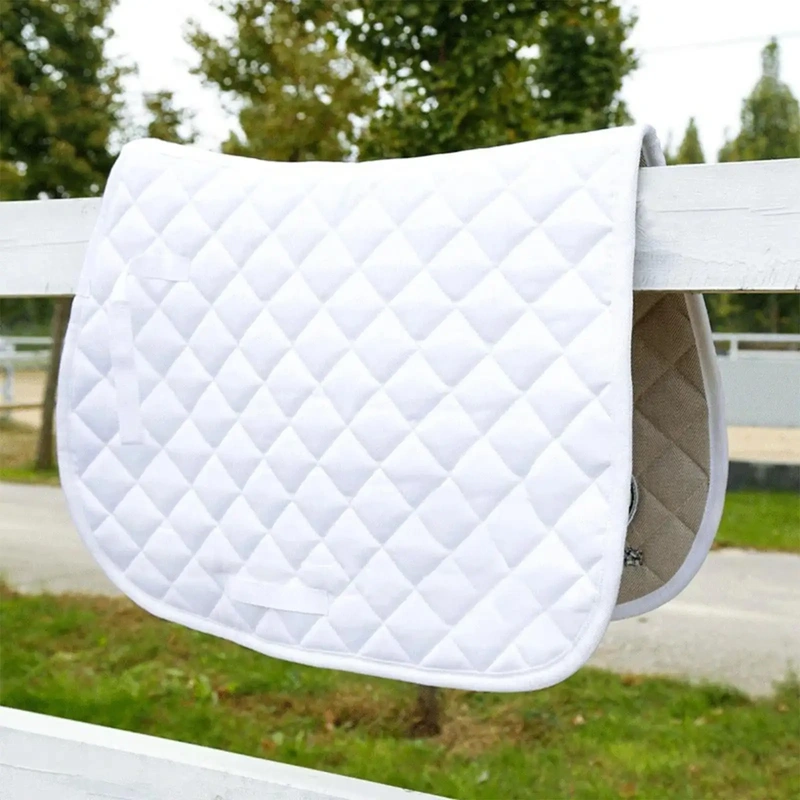 non-slip-cotton-horsesaddlepad-for-dressage-banner-1 White quilted horse saddle pad hanging on a fence in a riding arena