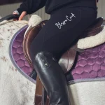 Black riding leggings on a rider sitting on a horse saddle pad