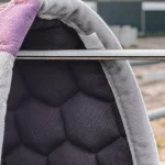Horse saddle pad with hexagonal padding hanging on a fence rail